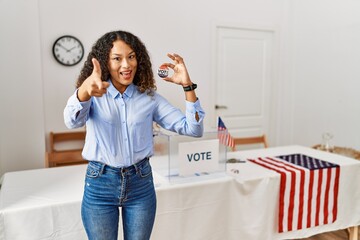 Beautiful hispanic woman standing by at political campaign by voting ballot pointing fingers to camera with happy and funny face. good energy and vibes.