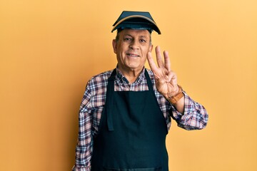 Handsome senior man with grey hair wearing welding protection mask showing and pointing up with fingers number three while smiling confident and happy.