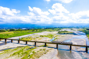 北アルプスを背景に常願寺川を渡る富山地方鉄道本線の普通列車	