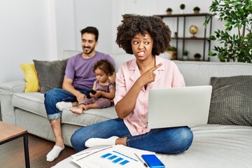 Mother of interracial family working using computer laptop at home pointing aside worried and nervous with forefinger, concerned and surprised expression