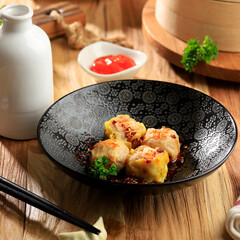Mini Chinese Dim Sum with Chilli Oil on a Black Bowl Above Wooden Table