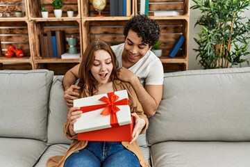 Young couple smiling happy sitting on the sofa surprise with anniversary gift at home.