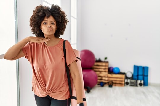 African american woman with afro hair holding yoga mat at pilates room cutting throat with hand as knife, threaten aggression with furious violence