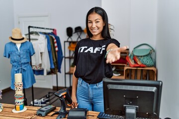Young hispanic woman working as staff at retail boutique smiling cheerful offering palm hand giving...