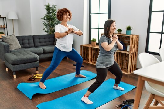 Mature Mother And Down Syndrome Daughter Doing Exercise At Home. Stretching At The Living Room