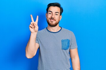 Fototapeta premium Handsome caucasian man with beard wearing casual striped t shirt showing and pointing up with fingers number two while smiling confident and happy.