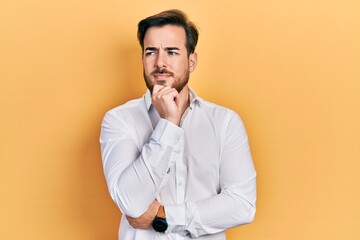 Handsome caucasian man with beard wearing business white shirt thinking concentrated about doubt with finger on chin and looking up wondering