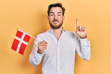 Handsome caucasian man with beard holding denmark flag smiling with an idea or question pointing...