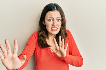 Young brunette woman wearing casual clothes afraid and terrified with fear expression stop gesture with hands, shouting in shock. panic concept.