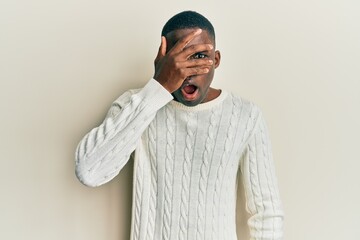 Young african american man wearing casual clothes peeking in shock covering face and eyes with hand, looking through fingers with embarrassed expression.