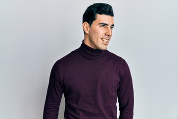 Handsome hispanic man wearing turtleneck sweater looking to side, relax profile pose with natural face and confident smile.