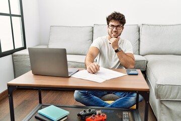 Hispanic man doing papers at home thinking worried about a question, concerned and nervous with hand on chin
