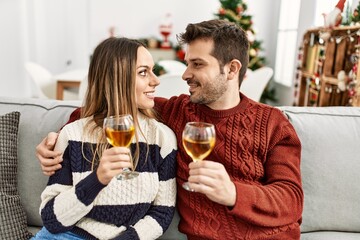 Young hispanic couple smiling happy toasting with champagne sitting on the sofa at home.