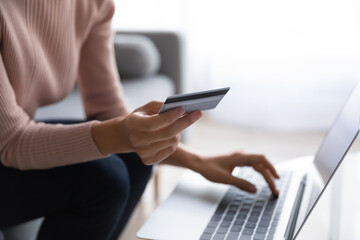 Female customer holds credit card use laptop do shopping buy on internet close up cropped view....