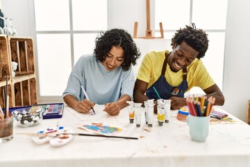 African american artist couple smiling happy painting sitting on the table at art studio.