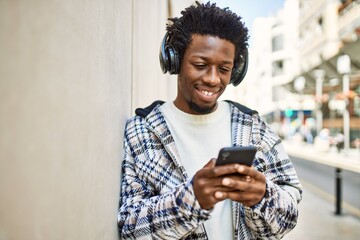 Fototapeta premium Handsome black man with afro hair wearing headphones and listening to music using smartphone