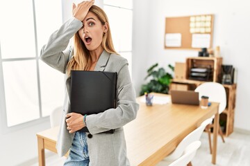 Blonde business woman at the office surprised with hand on head for mistake, remember error. forgot, bad memory concept.
