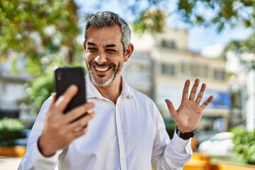 Middle age grey-haired man doing video call using smartphone at the city.