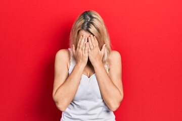 Beautiful caucasian blonde woman wearing casual white t shirt with sad expression covering face with hands while crying. depression concept.