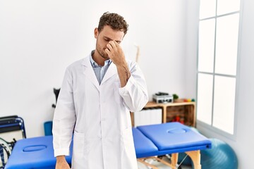 Obraz premium Handsome young man working at pain recovery clinic tired rubbing nose and eyes feeling fatigue and headache. stress and frustration concept.