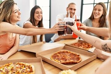 Group of young friends smiling happy eating italian pizza and toasting with cola beverage at home.