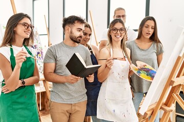Group of young paint students smiling happy and looking draw of partner at art studio.