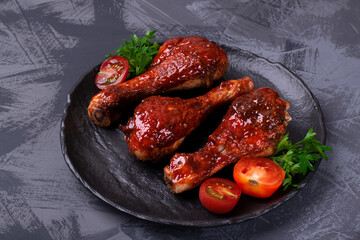 Chicken drumsticks roasted in sweet and spicy tomato glazing served on the stone plate on gray table