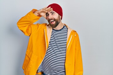 Caucasian man with beard wearing yellow raincoat very happy and smiling looking far away with hand...