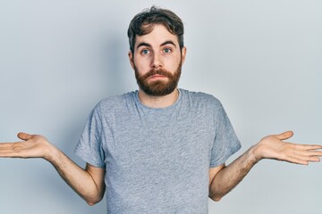 Caucasian man with beard wearing casual grey t shirt clueless and confused expression with arms and...