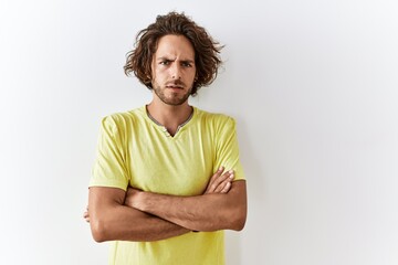 Young hispanic man standing over isolated background skeptic and nervous, disapproving expression on face with crossed arms. negative person.