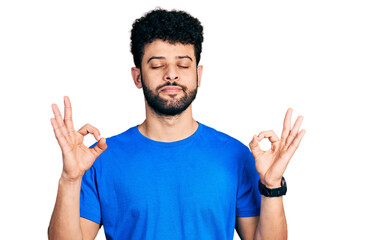 Young arab man with beard wearing casual blue t shirt relaxed and smiling with eyes closed doing meditation gesture with fingers. yoga concept.