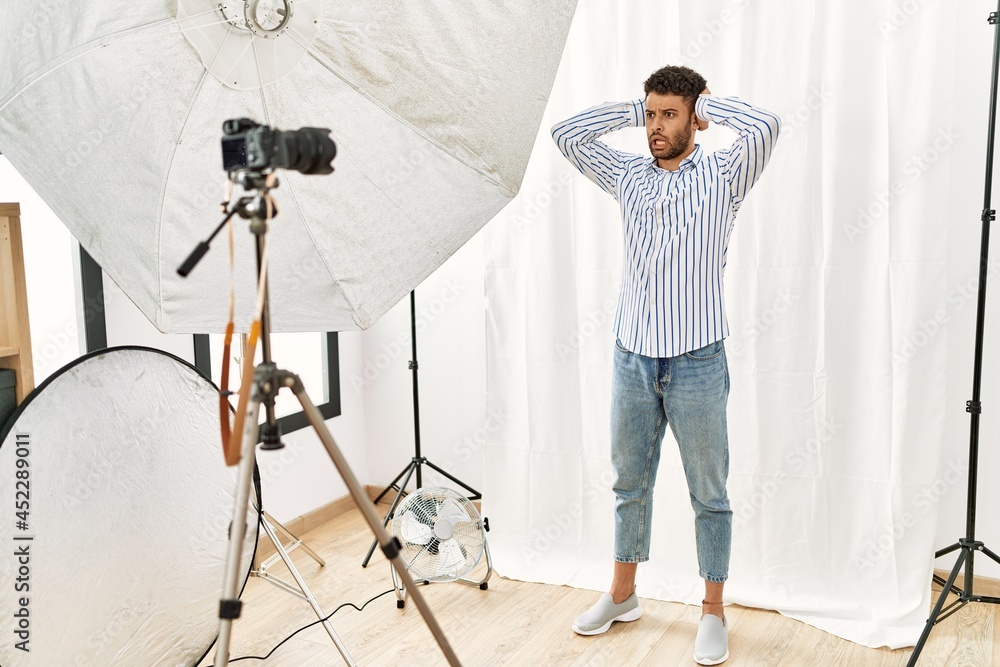 Poster arab young man posing as model at photography studio crazy and scared with hands on head, afraid and