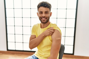 Arab young man getting vaccine showing arm with band aid looking positive and happy standing and smiling with a confident smile showing teeth - obrazy, fototapety, plakaty
