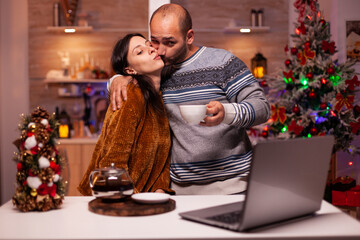 Happy boyfriend kissing girlfriend while discussing with remote friends during online videocall meeting conference using laptop. Cheerful family smiling enjoying christmas holiday together