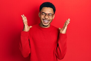 Naklejka premium Young african american man wearing casual clothes and glasses celebrating mad and crazy for success with arms raised and closed eyes screaming excited. winner concept