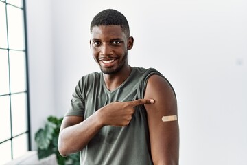 Young african american man getting vaccine showing arm with band aid smiling happy pointing with...