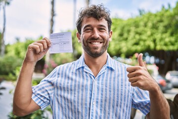 Young handsome man holding covid record card smiling happy and positive, thumb up doing excellent...