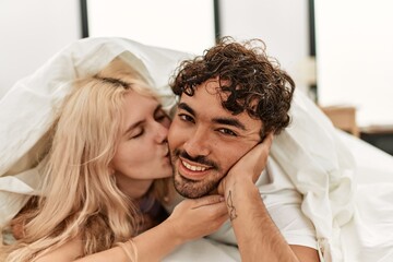 Young beautiful couple smiling happy covering with sheet lying on the bed.