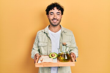 Young hispanic man holding tray with breakfast food smiling with a happy and cool smile on face....