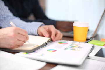 Image of two young businessmen using touchpad and note at meeting