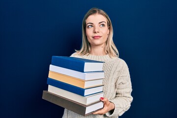 Beautiful caucasian woman holding a pile of books smiling looking to the side and staring away thinking.