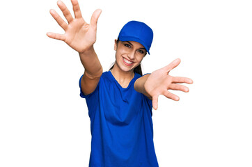 Young hispanic girl wearing delivery courier uniform looking at the camera smiling with open arms for hug. cheerful expression embracing happiness.