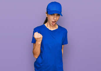Young hispanic girl wearing delivery courier uniform angry and mad raising fist frustrated and furious while shouting with anger. rage and aggressive concept.
