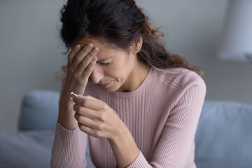 Close up millennial Hispanic woman closed eyes crying sit on sofa takes off wed ring goes through...