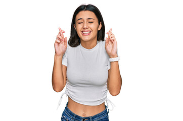Obraz na płótnie Canvas Young hispanic girl wearing casual white t shirt gesturing finger crossed smiling with hope and eyes closed. luck and superstitious concept.