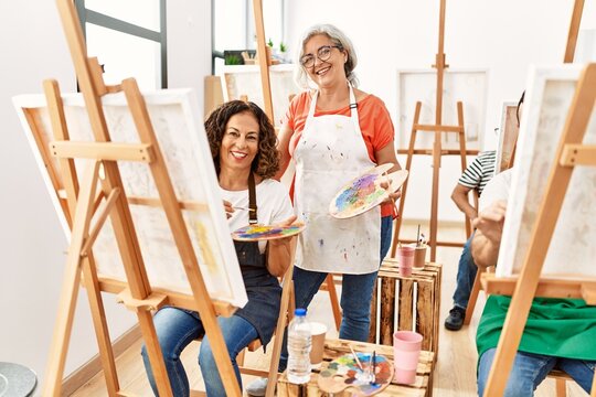 Group of middle age draw students drawing at art studio. Teacher and student woman smiling happy looking to the camera.