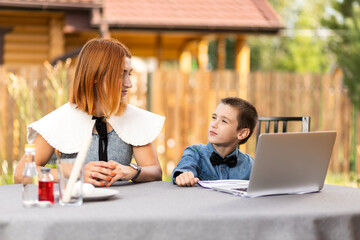 mom teaches the child at home in the garden, home schooling. Mom helps her son do his homework, stress. Online school lessons via laptop