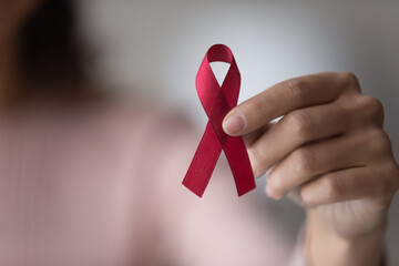 Close up focus on red ribbon in female hands, woman standing indoor promote annual regular health...