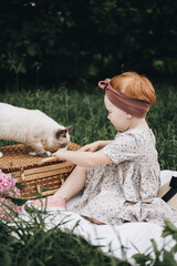 Cute red headed girl with beautiful cat in the summer park. Child and the pet. Little friend. Summer picnic.