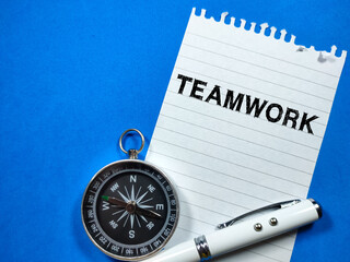 Text TEAMWORK writing on notepaper with pen and compass on blue background.